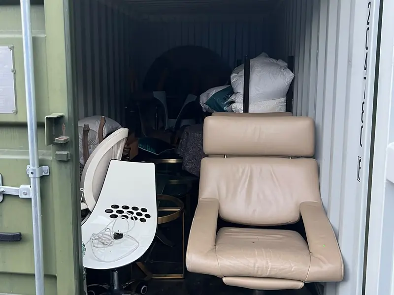Leather armchair, dining chairs and bedding loaded inside a steel storage container