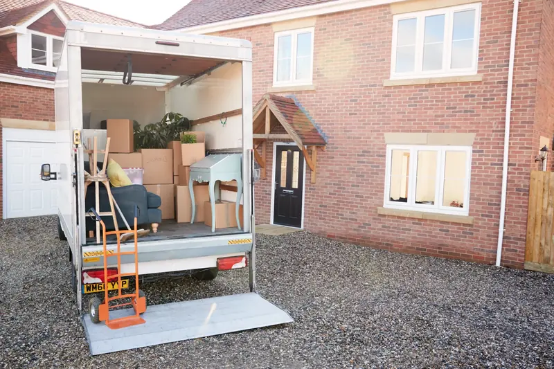 Removal van with its tail lift down, loaded with boxes and furniture outside a brick house